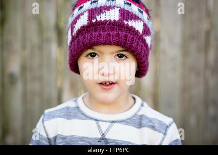 Close-up ritratto di carino ragazzo indossa knit hat mentre in piedi contro la recinzione in cantiere Foto Stock