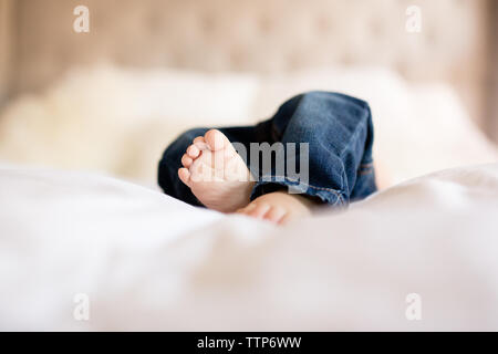 Baby dita dei piedi che spuntavano da jeans denim sul letto in ambienti interni Foto Stock