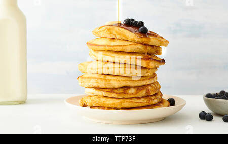 Pila di pancake con mirtilli e sciroppo d'acero nella piastra sulla tavola Foto Stock