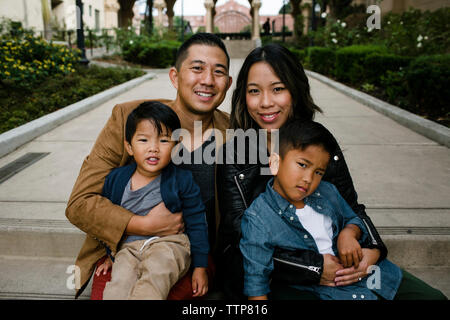 Ritratto di sorridere i genitori con figli carino seduto sui gradini al Balboa Park Foto Stock