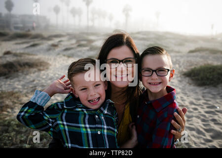 Ritratto di felice madre con graziosi figli a beach contro sky durante il tramonto Foto Stock