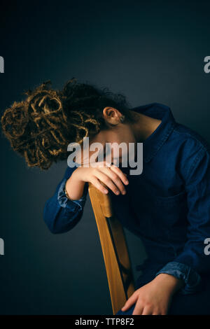 Triste donna appoggiata su una sedia schienale contro sfondo blu Foto Stock