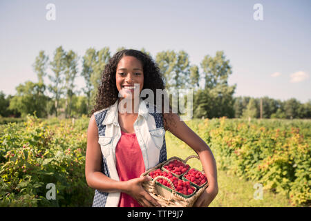 Ritratto di donna sorridente cestello di contenimento con lamponi nel campo Foto Stock