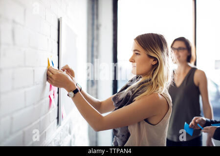 donna d'affari che appende appunti sul muro nell'ufficio creativo Foto Stock