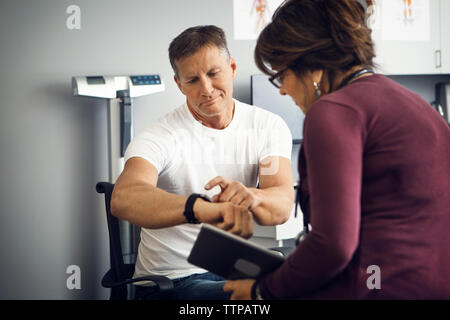 Paziente di sesso maschile che mostra orologio da polso femminile al medico in clinica Foto Stock