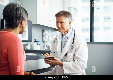 Voce maschile medico iscritto negli appunti durante la discussione con il paziente di sesso femminile in clinica Foto Stock
