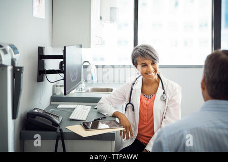 Felice medico donna parlare al paziente di sesso maschile in clinica Foto Stock