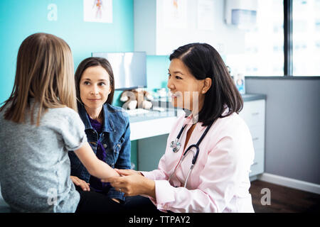 Donna sorridente medico esaminando la mano della bambina in clinica Foto Stock