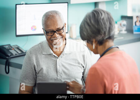 Felice senior paziente di sesso maschile di parlare al medico donna in clinica Foto Stock