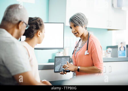 Medico donna spiegando x-ray al padre e figlia in clinica Foto Stock