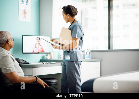 Vista laterale del medico donna discutendo con un collega sulla chiamata in conferenza mentre il paziente seduto in clinica Foto Stock