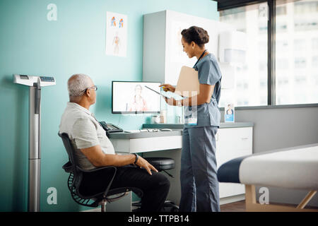 Medico donna discutendo con un collega sulla chiamata in conferenza mentre il paziente seduto in clinica Foto Stock
