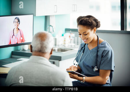 Felice medico donna utilizzando computer tablet durante la seduta con il paziente in clinica Foto Stock