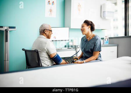Felice medico femmina maschio di controllo pressione del sangue del paziente in clinica Foto Stock