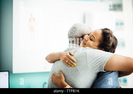 Vista laterale del medico donna abbracciando il senior paziente di sesso maschile in clinica Foto Stock