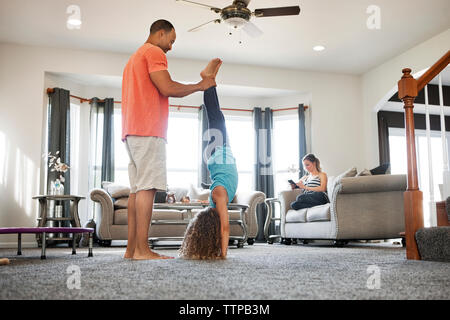 Padre aiutando la figlia facendo handstand nel salotto di casa Foto Stock