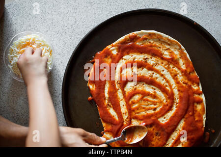 Immagine ritagliata di padre e figlia di applicare in salsa di pane pizza Foto Stock