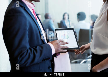 uomo d'affari che mostra un grafico a torta sul tablet al collega in ufficio Foto Stock