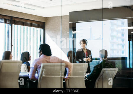 donna d'affari che tiene una presentazione durante una riunione vista attraverso una finestra di vetro Foto Stock