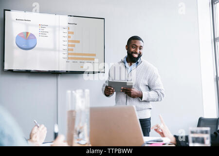 Imprenditore sorridente azienda computer tablet per spiegare i grafici nella riunione a board camera Foto Stock