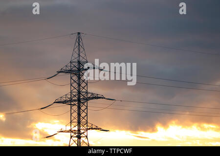 Silhouette della linea elettrica ad alta tensione supporti con fili elettrici sullo sfondo del cielo di sera con nuvole. Linee di trasmissione di energia elettrica Foto Stock