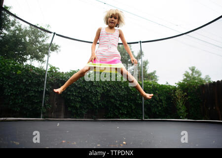 Angolo basso ritratto della ragazza di saltare sul trampolino presso il park contro il cielo chiaro Foto Stock