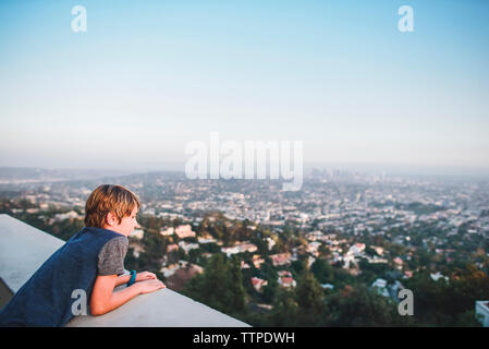 Angolo di Alta Vista del ragazzo che guarda al paesaggio mentre appoggiata sulla parete di ritegno contro il cielo a terrazza Foto Stock