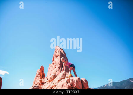Basso angolo vista della ragazza arrampicata su roccia formazione contro sky Foto Stock
