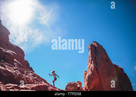 Basso angolo vista della ragazza spensierata arrampicata su roccia formazione contro sky Foto Stock