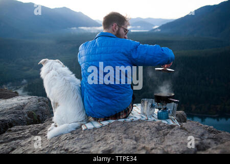 Vista posteriore dell'uomo con il cane di cottura degli alimenti sulle montagne Foto Stock