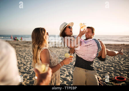 Allegro uomo che porta femmina azienda amico bere un bicchiere sulla spiaggia Foto Stock