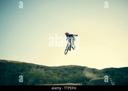 Basso angolo vista del biker eseguendo stunt contro il cielo chiaro Foto Stock