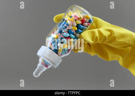 Mano nel guanto tenendo il biberon pieno di pillole su sfondo grigio Foto Stock