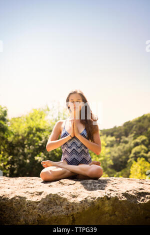 Adolescente meditando sulla sommità della roccia contro il cielo chiaro al forest Foto Stock