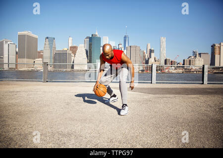 Lunghezza completa dell'uomo gioca con la pallacanestro sul lungomare nei confronti dello skyline della città Foto Stock