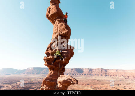 Gli escursionisti femmina arrampicata su roccia formazione contro il cielo chiaro Foto Stock