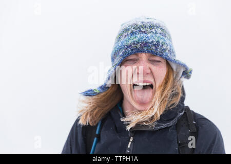 Close-up di giocosa donna che indossa abiti caldi spuntavano lingua durante il periodo invernale Foto Stock