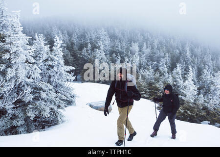 Lunghezza completa di amici sorridente con escursioni poli ad esplorare la foresta durante il periodo invernale Foto Stock