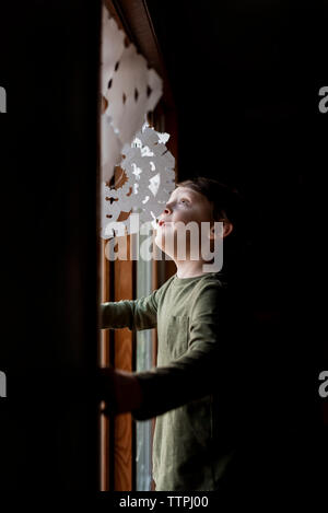 Un piccolo ragazzo alla ricerca fino a carta fiocchi di neve in una finestra Foto Stock