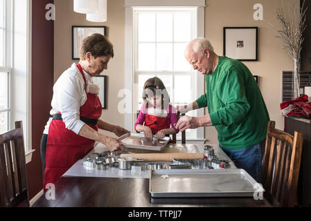 La nipote aiutando i nonni nel rendere gingerbread cookies a casa Foto Stock