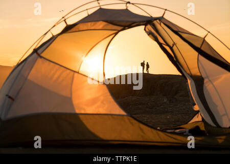 Vista in lontananza giovane permanente sulla formazione di roccia visto attraverso la tenda durante il tramonto Foto Stock