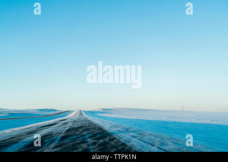 Vista panoramica della strada in mezzo paesaggi innevati contro il cielo chiaro Foto Stock