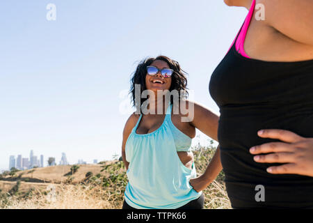 Donna felice guardando amico femmina mentre in piedi contro il cielo chiaro Foto Stock