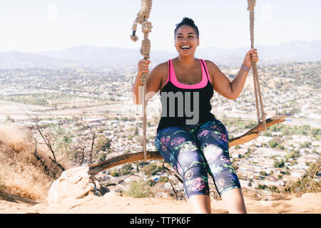 Donna allegra basculante in swing corda contro townscape Foto Stock