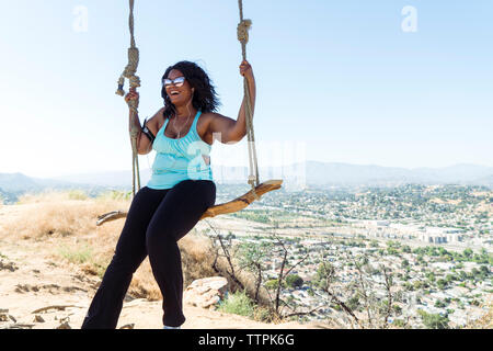 Donna felice basculante in swing corda contro townscape Foto Stock