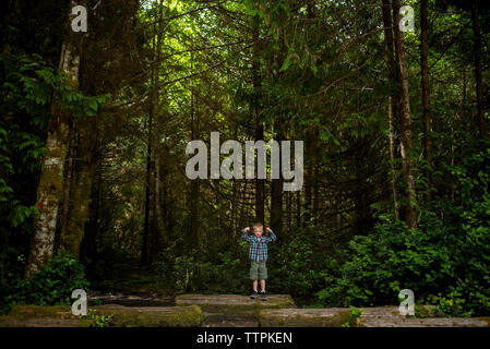 Ritratto di ragazzo flettendo i muscoli mentre si sta in piedi sul log in foresta Foto Stock