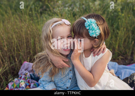 Angolo di Alta Vista della ragazza whispering in suor l orecchio mentre è seduto su una coperta in posizione di parcheggio Foto Stock