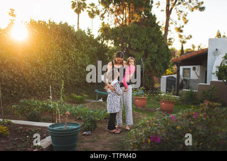 Madre con le figlie in piedi in cantiere contro il cielo durante il tramonto Foto Stock