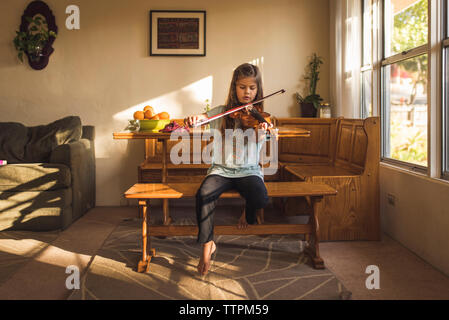 Ragazza suona il violino mentre è seduto sul sedile in legno a casa Foto Stock