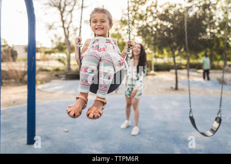 Felice madre spingendo carino figlia swinging presso il parco giochi Foto Stock